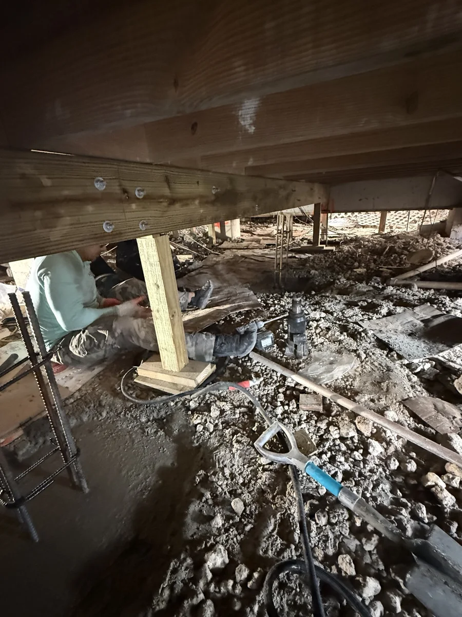 Crew member working under a raised home around temporary supports and framing.