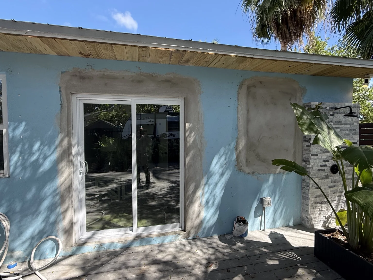 White sliding glass patio door installed in a newly reconfigured exterior wall of a blue house, with stucco patching still in progress.